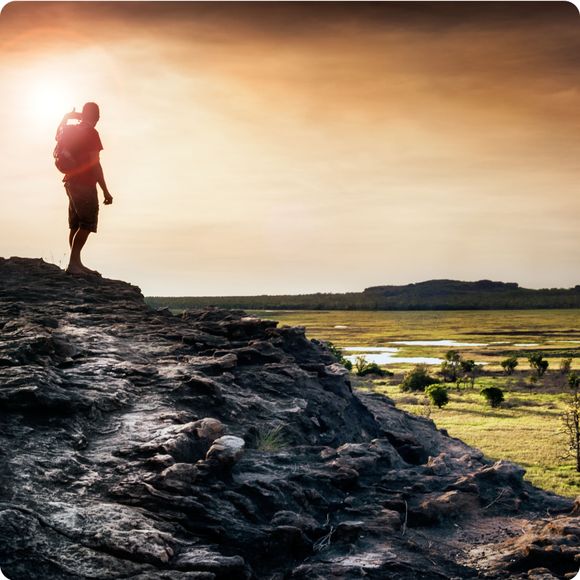 Lone figure watches the sunset from Ubirr rock looking down at the Nadab floodplains. Northern Territory, Australia.